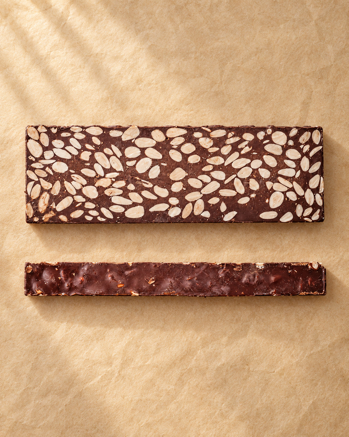 Vista desde arriba de una pieza de turrón de chocolate 60 % con almendras de Can Soler junto a una loncha lateral