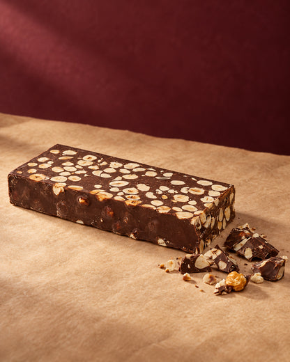 Barra de turrón de chocolate 60 % con avellanas de Can Soler junto a trozos partidos y avellanas sueltas