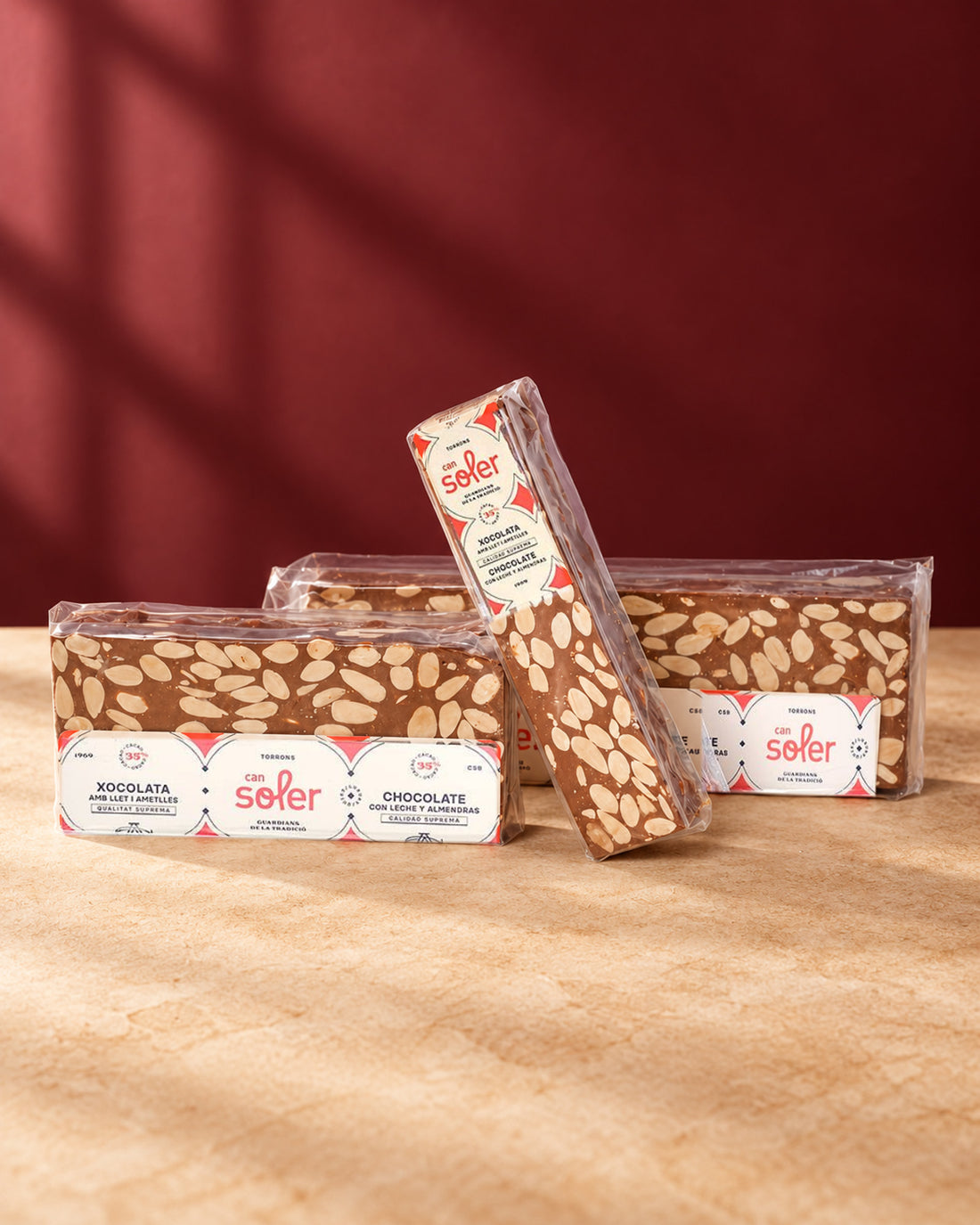 Tres paquetes de turrón de chocolate con leche y almendras de Can Soler con su etiqueta, uno de ellos de pie