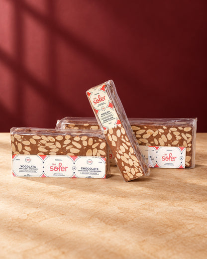 Tres paquetes de turrón de chocolate con leche y almendras de Can Soler con su etiqueta, uno de ellos de pie
