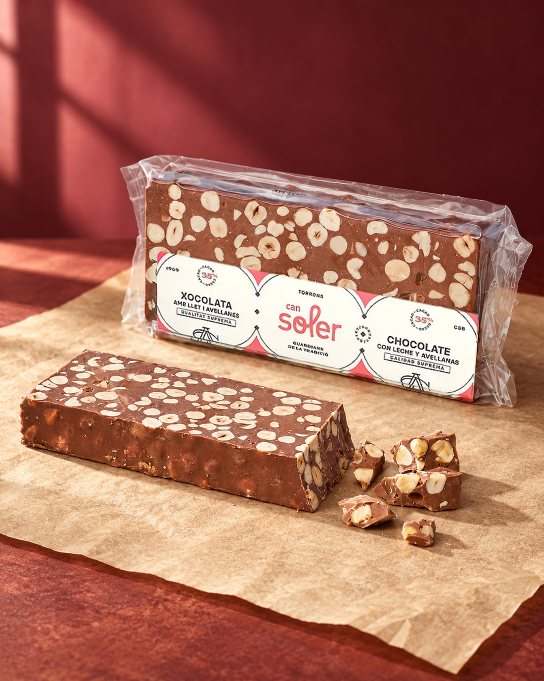 Turrón de chocolate con leche y avellanas de Can Soler en su envase, junto a una barra sin envase y trozos partidos