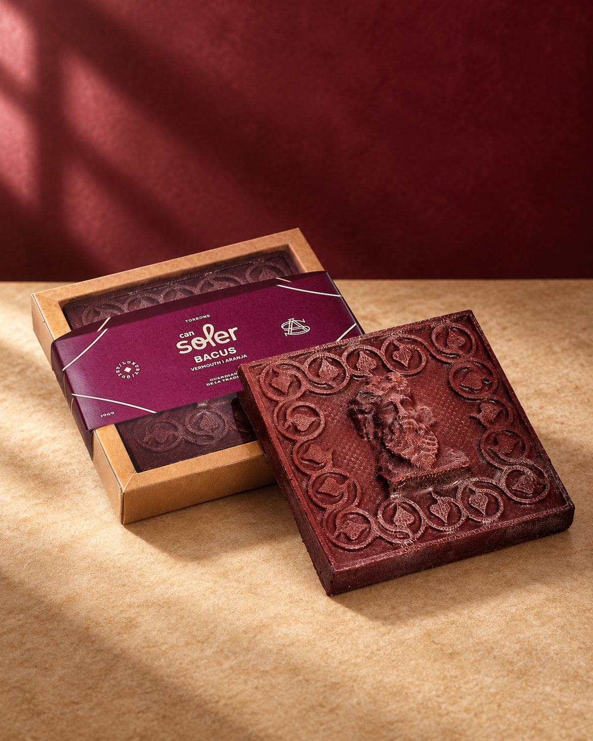 Chocolate de Museo «Bacus» de Can Soler: placa con relieve de un busto barbado y orla de hojas junto a su estuche con faja morada