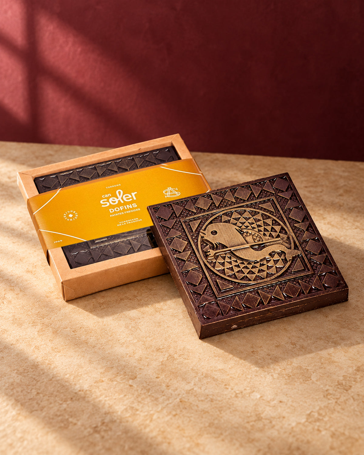 Chocolate de Museo Els Dofins de Can Soler: tableta con relieve de un pez y triángulos junto a su caja con faja naranja