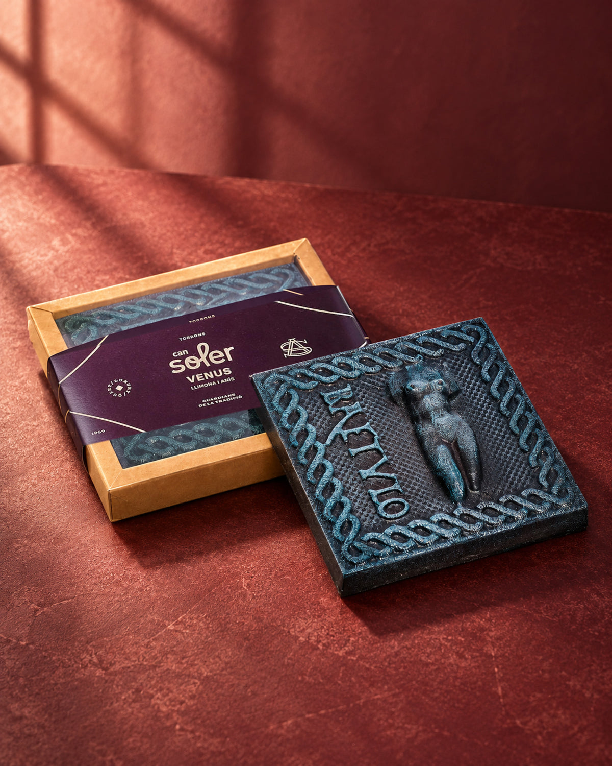 Caja de Chocolate de Museo Venus de Can Soler con faja morada junto a una placa de chocolate con el relieve de una Venus