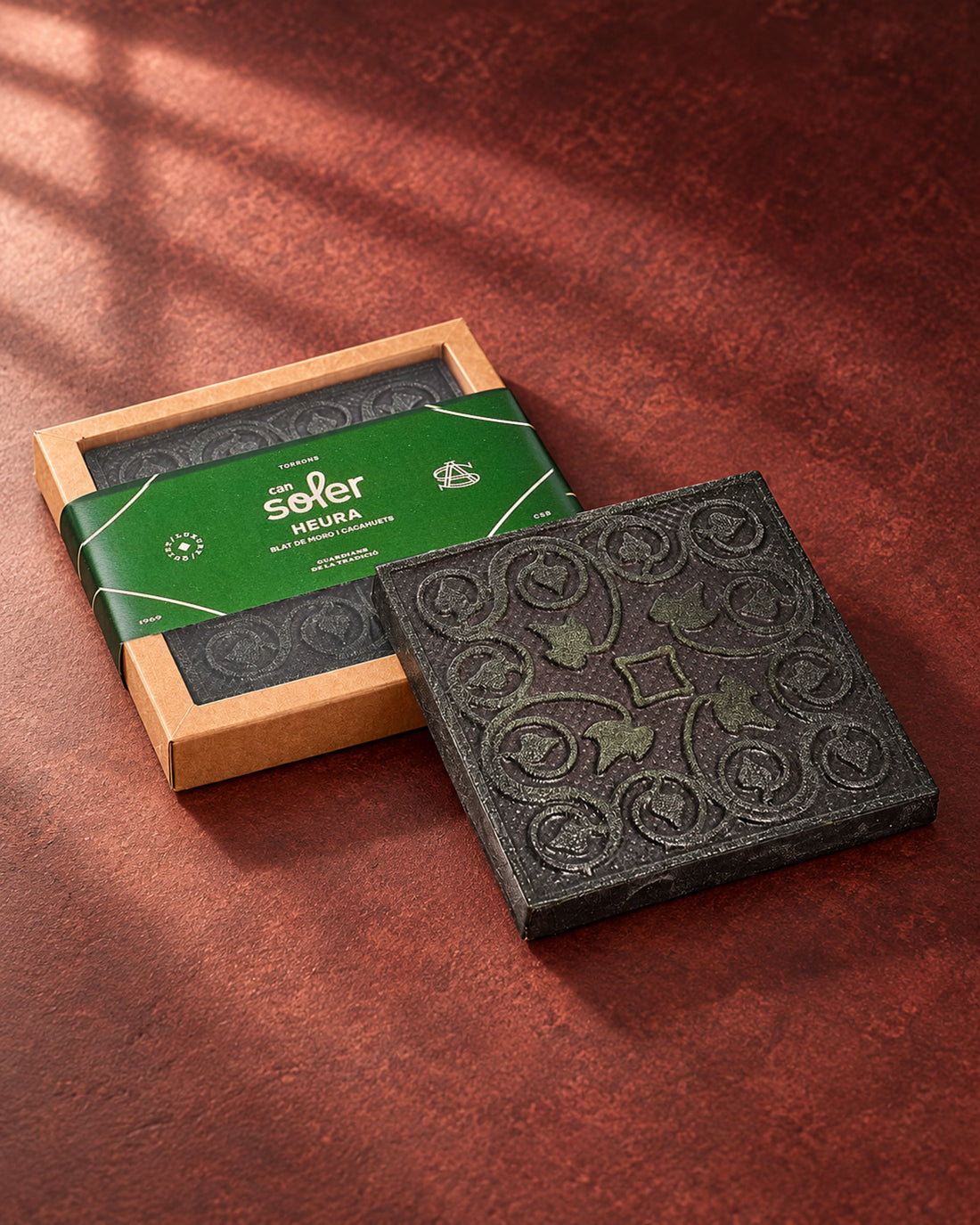 Chocolate de Museo «L'Heura» de Can Soler: placa con relieve de hojas de hiedra y espirales junto a su estuche con faja verde