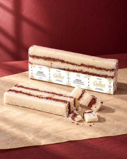 Turrón de coco con chocolate de Can Soler en su envase, con una barra en capas y trozos cortados delante