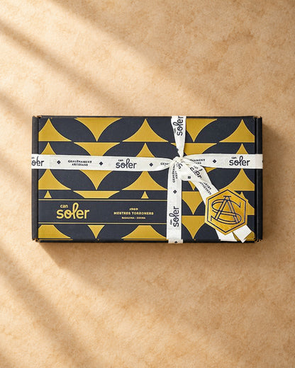 Caja negra y dorada del pack degustación «Somos 2 en casa» de Can Soler, cerrada con cinta blanca y sello de la marca