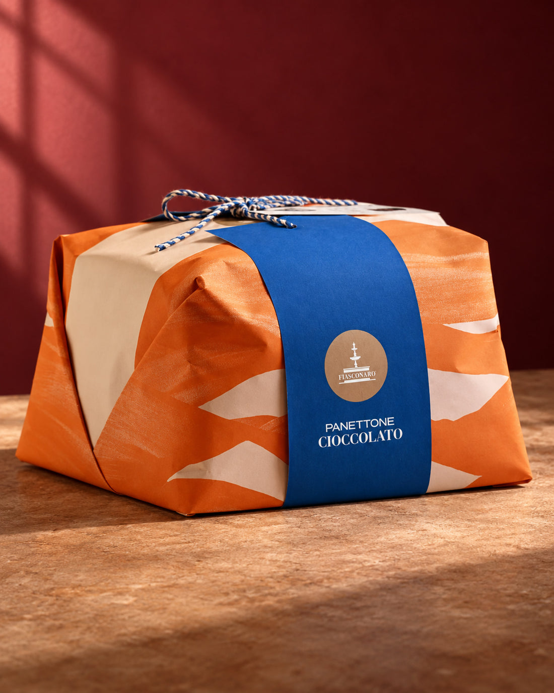 Panettone Fiasconaro de chocolate envuelto en papel naranja y crema con faja azul y asas de cordón