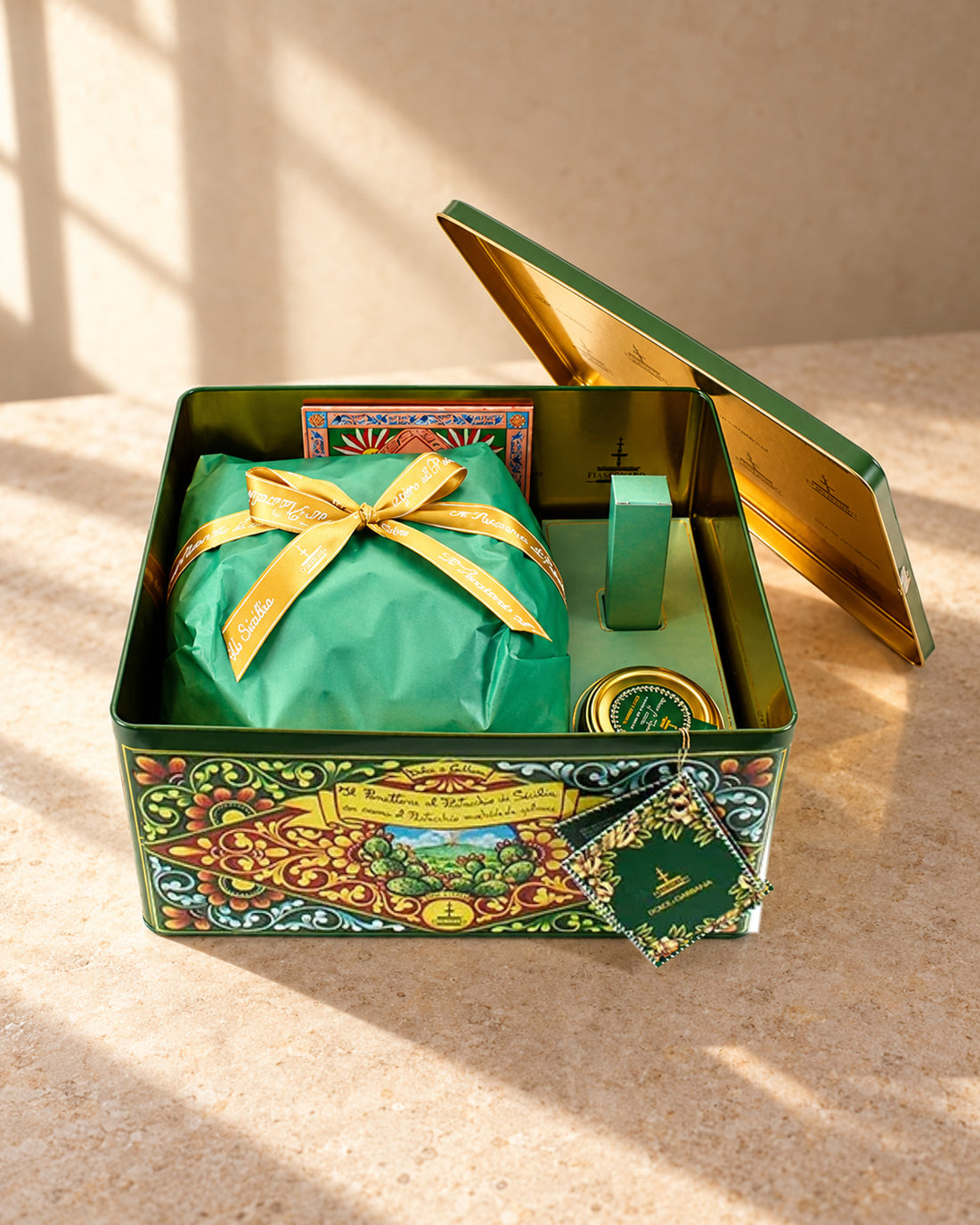 Lata Dolce&Gabbana abierta con el panettone Fiasconaro de pistacho envuelto en papel verde con lazo dorado y un tarrito