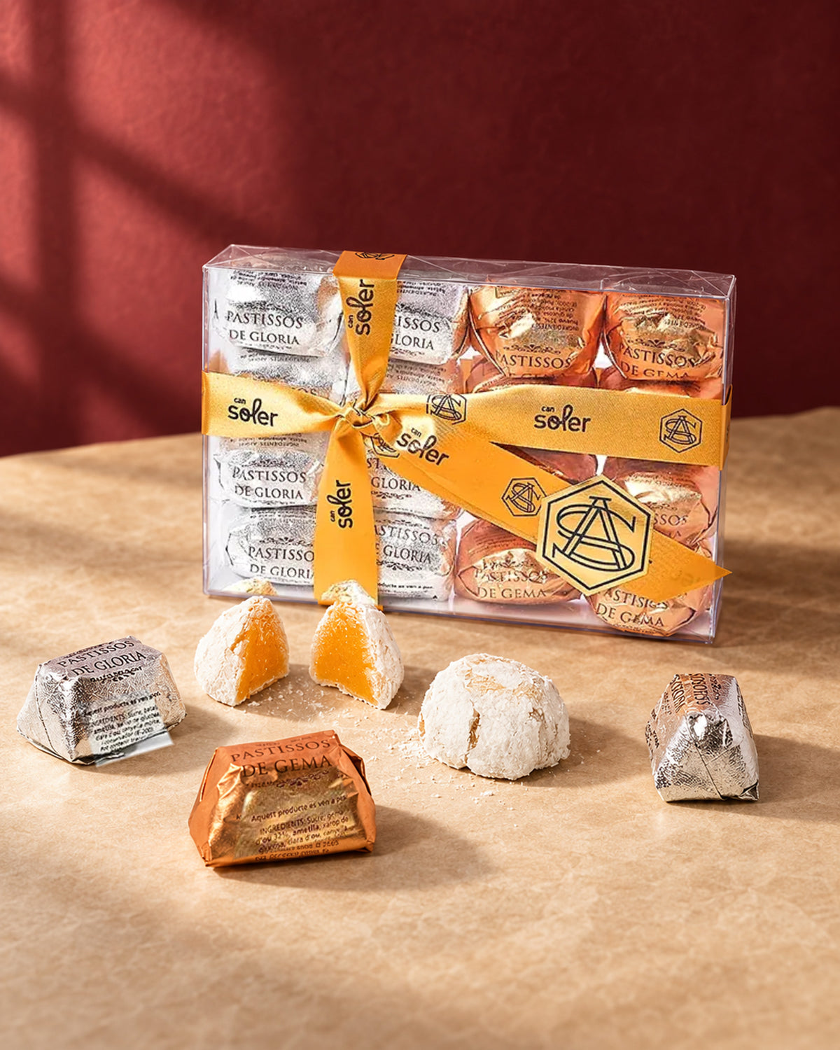 Caja de pastelitos de mazapán variados Can Soler con cinta dorada, piezas envueltas en plateado y cobre y una partida