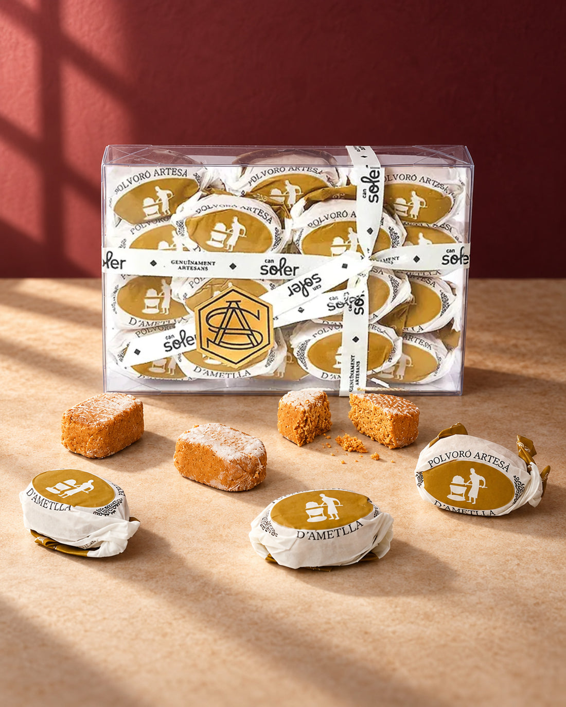 Caja transparente de polvorones de almendra de Can Soler con cinta blanca, junto a polvorones envueltos y sin envolver