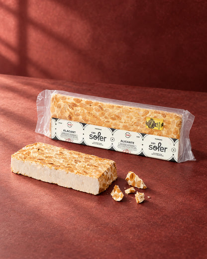 Turrón de Alicante D.O. Alicante de Can Soler: barra sin envase, trozos partidos y el paquete con su etiqueta detrás