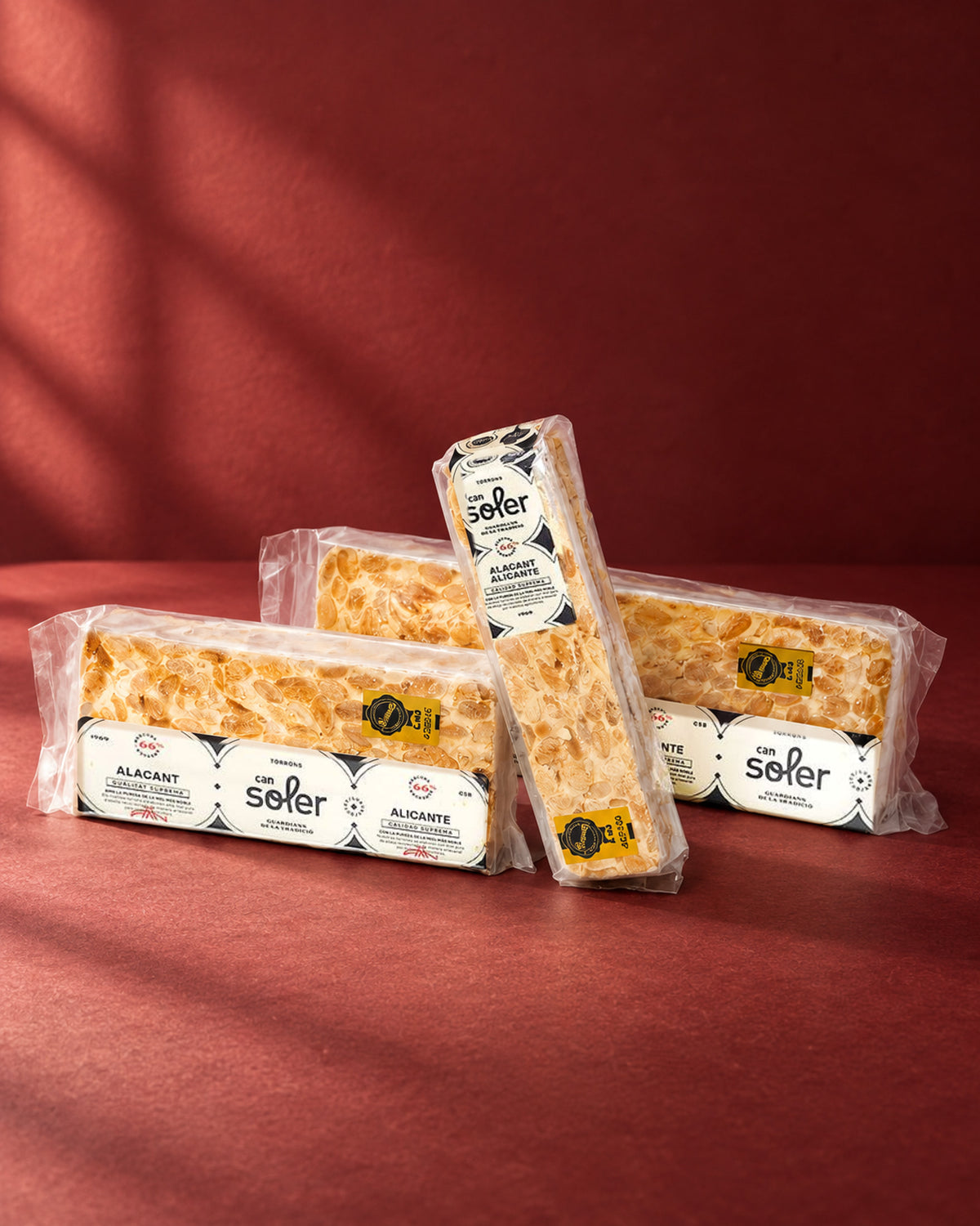 Tres paquetes de turrón de Alicante D.O. Alicante de Can Soler con su etiqueta, uno apoyado en vertical