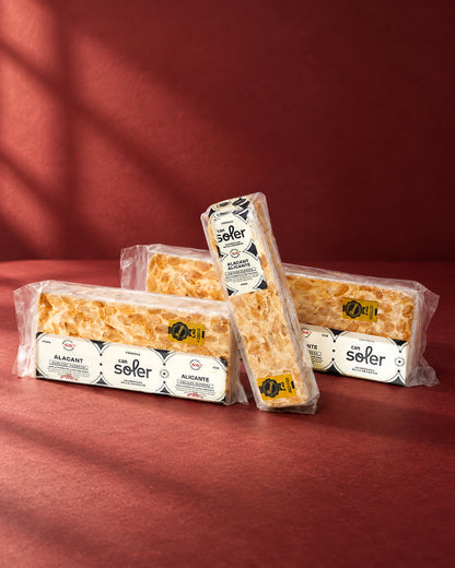 Tres paquetes de turrón de Alicante D.O. Alicante de Can Soler con su etiqueta, uno apoyado en vertical