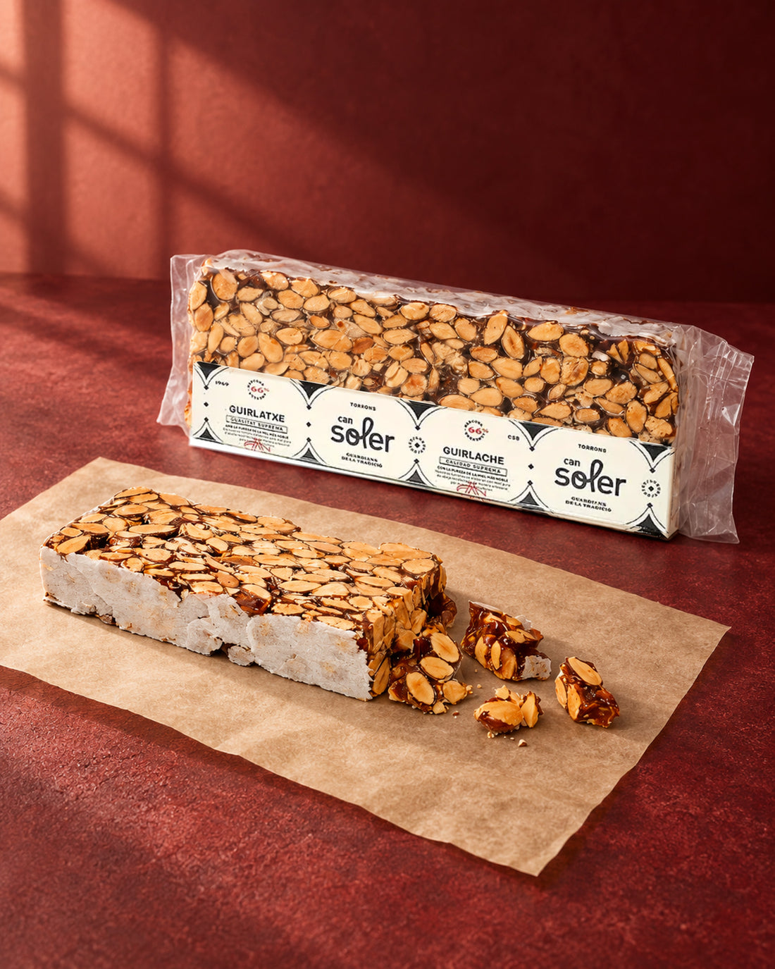 Turrón guirlache de Can Soler en su envase con etiqueta y una barra sin envasar con trozos partidos de almendra y caramelo