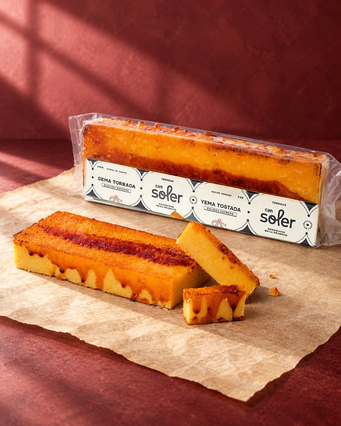Turrón de yema tostada de Can Soler en su envase, con una barra caramelizada sin envase y trozos cortados delante