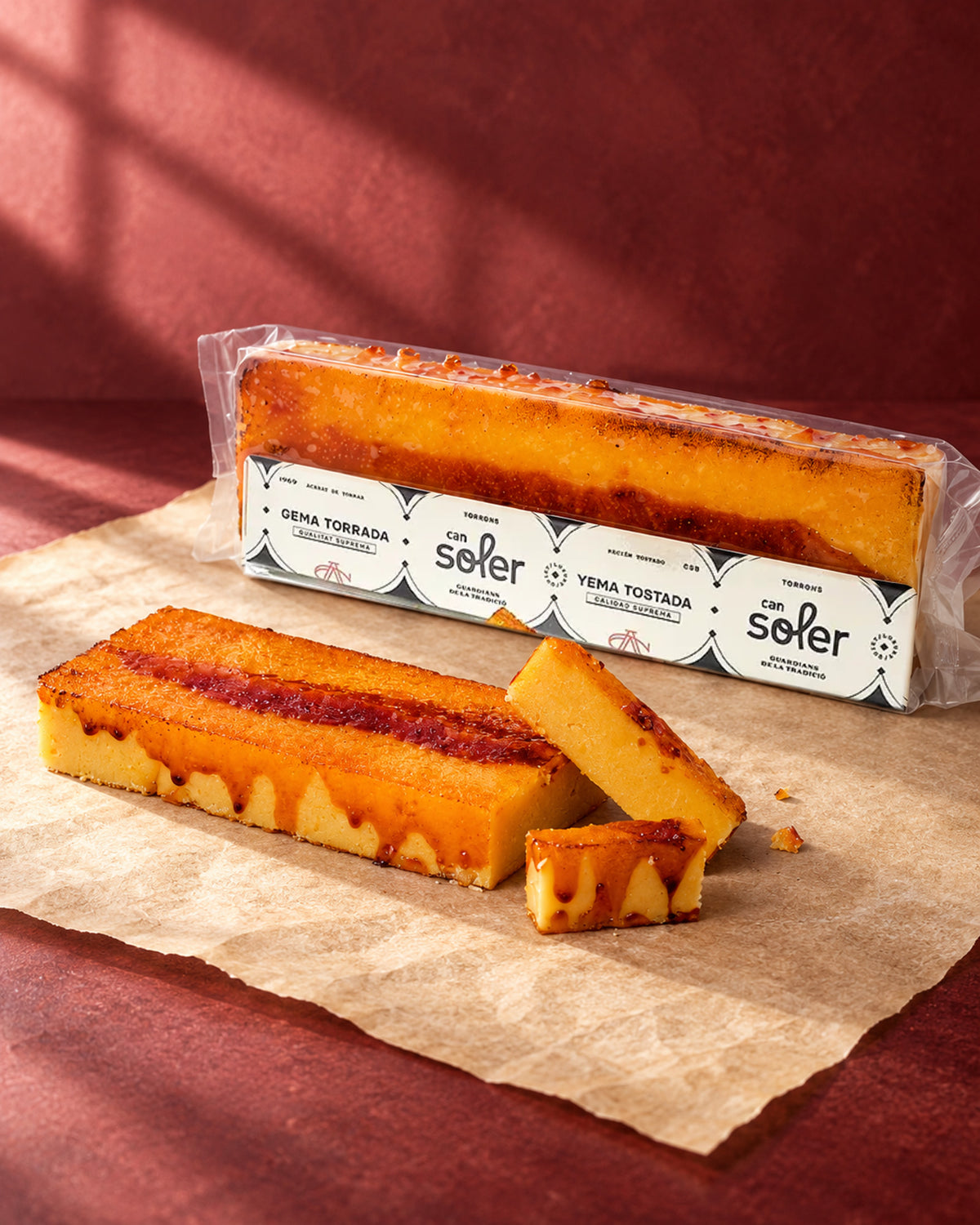 Turrón de yema tostada de Can Soler en su envase, con una barra caramelizada sin envase y trozos cortados delante